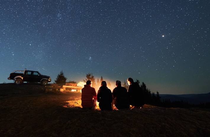 Friends on a unexpected adventure in the mountains gathered around a campfire under a starry sky