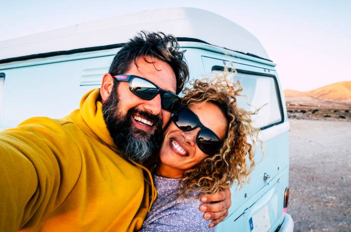 Couple taking a selfie in front of a camper during a celebration roadtrip