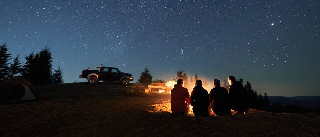 Vrienden op een onverwacht avontuur in de bergen verzameld rond een kampvuur onder een sterrenhemel.